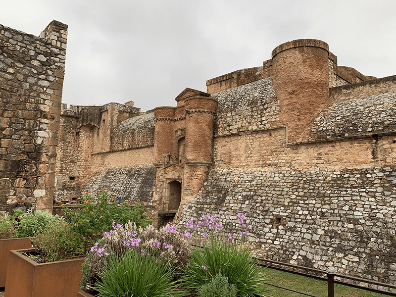 Ancient stone castle with tall walls, towers, and lush garden.