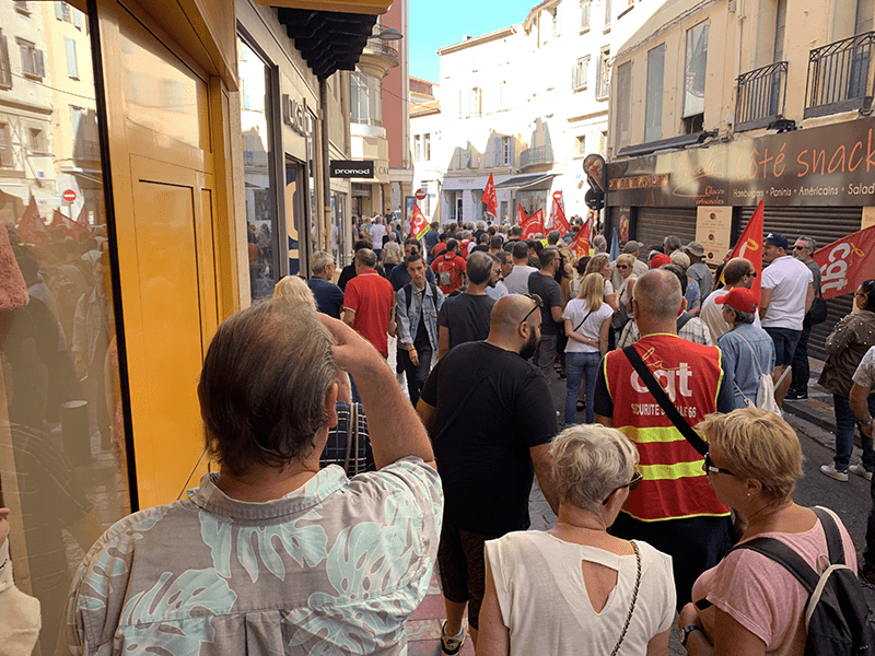 A crowd of people gathered in a European city street, with individuals holding red flags or banners.