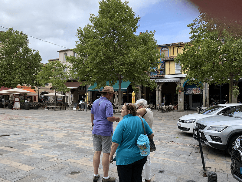 People standing in a small town square surrounded by buildings and parked cars.
