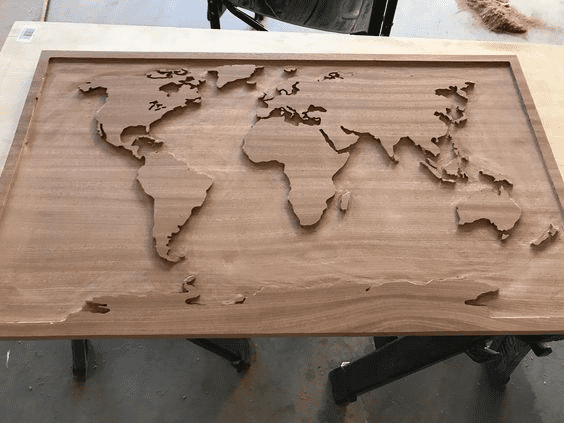 A wooden world map on a table with a light-colored wood finish and dark frame, set against a gray background.
