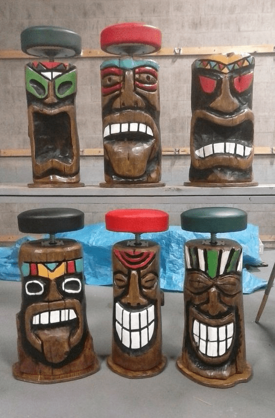 Intricately carved wooden totem poles with painted faces arranged on a gray floor.