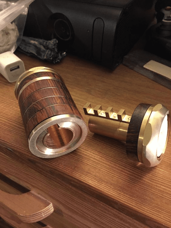 Dark wood grain finished cylinders with metal bands and teeth-like protrusions on a wooden surface.