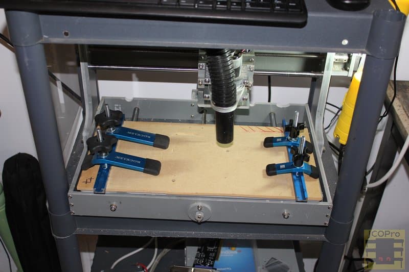 Rockler Deluxe Mini CNC Router setup with grey metal frame, beige platform and blue clamps.
