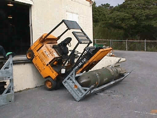 A forklift lifting a large cylindrical object near an open door in a yard with trees and a fence.