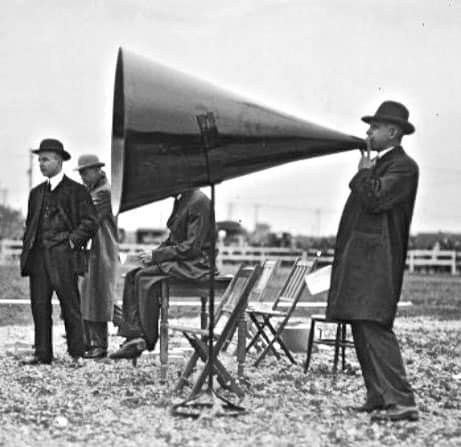 A man in a hat is using a megaphone to promote CNCCookbook's survey results for machine shop marketing.