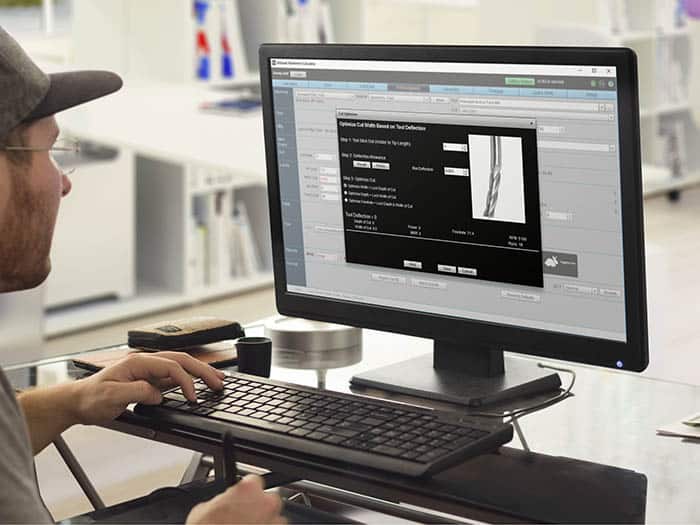 Man sitting at desk in front of computer monitors, focused on graphic with text, wearing casual clothing.