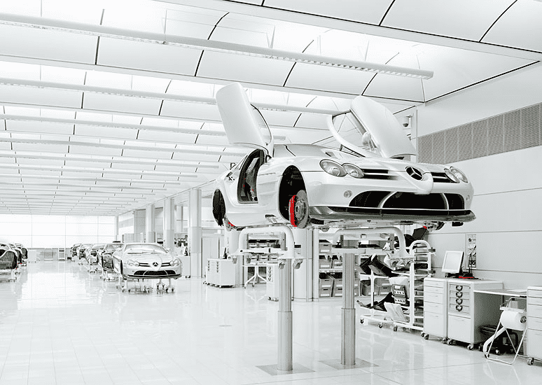Large, well-lit metal fabrication workshop with cars on hydraulic lifts.