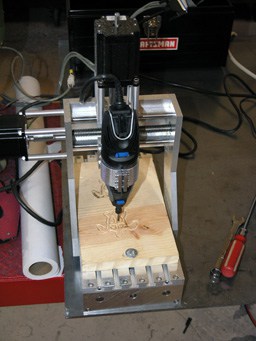 A small CNC router with black body and silver accents, blue button, and cutting tool.