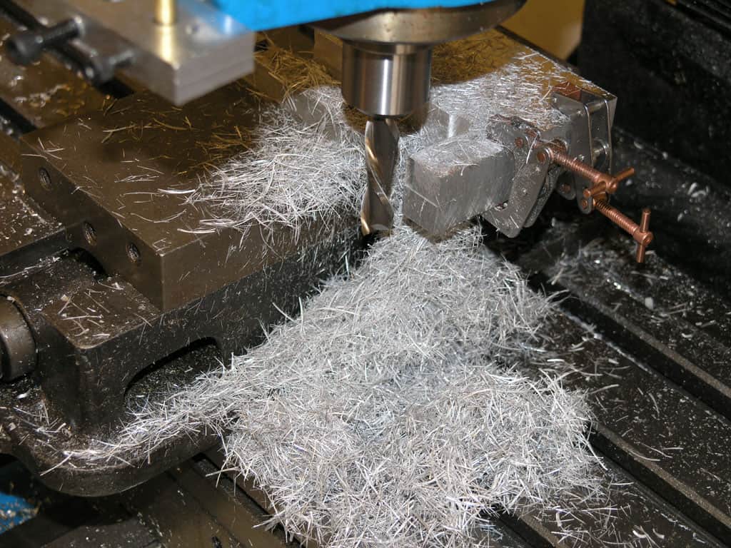 Metalworking machine with blue top, brown base, and metal components, surrounded by white shavings.