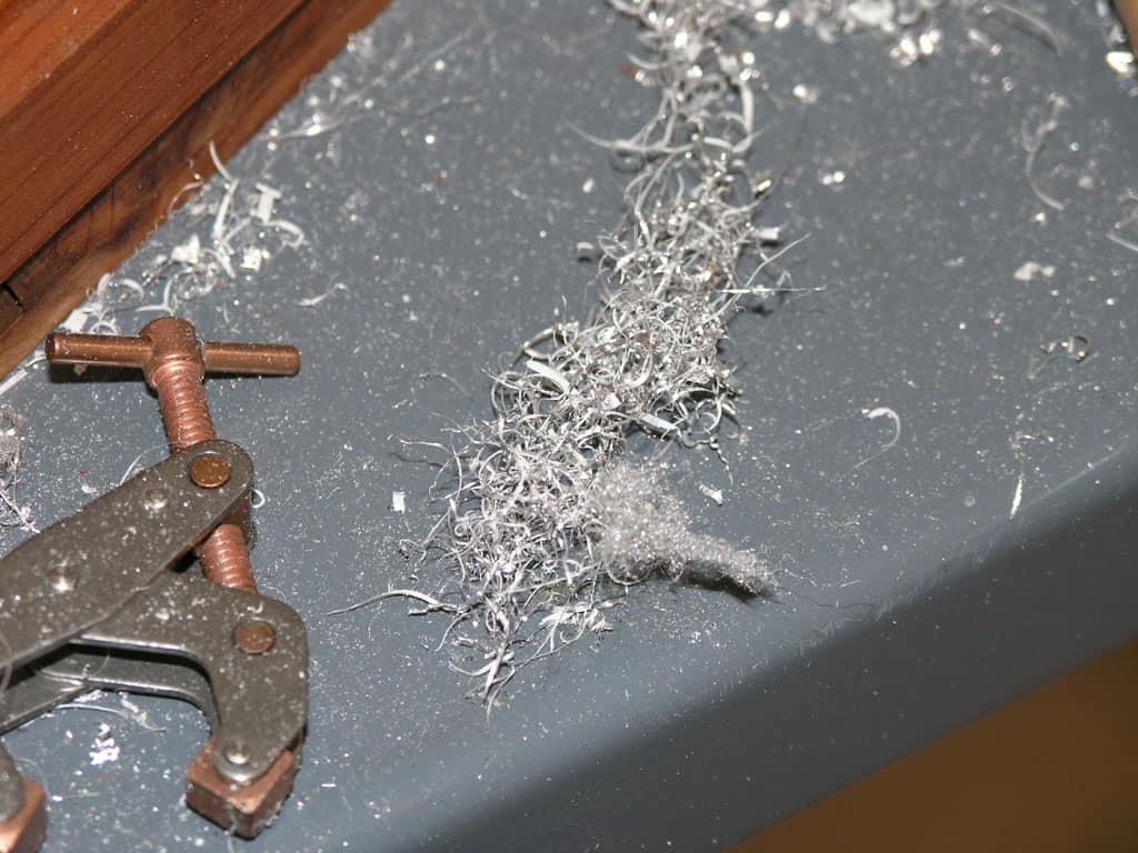 Metal shavings on a cluttered work surface with a copper-colored clamp.