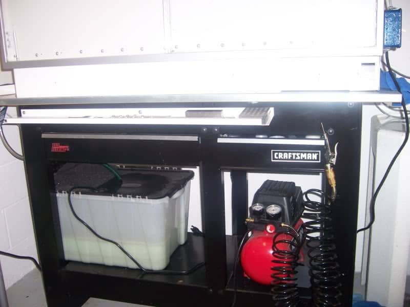 Black Craftsman air compressor with red tank and hose under workbench.