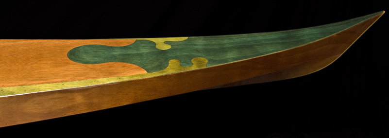 A wooden boat's stern with a curved hull, greenish-yellow paint, decorative starboard element, and horizontal waterline indicator.