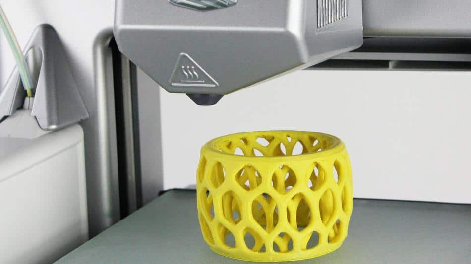 A yellow 3d printer is being used to make a cup.