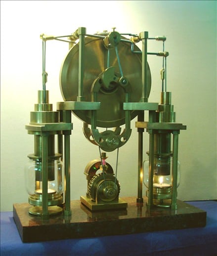 Brass clock with glass cylinders and wooden base.
