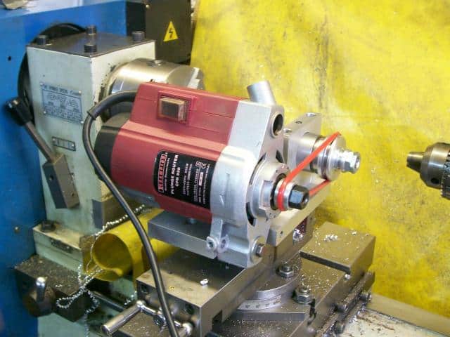 Red and silver metal lathe on blue table against yellow wall.
