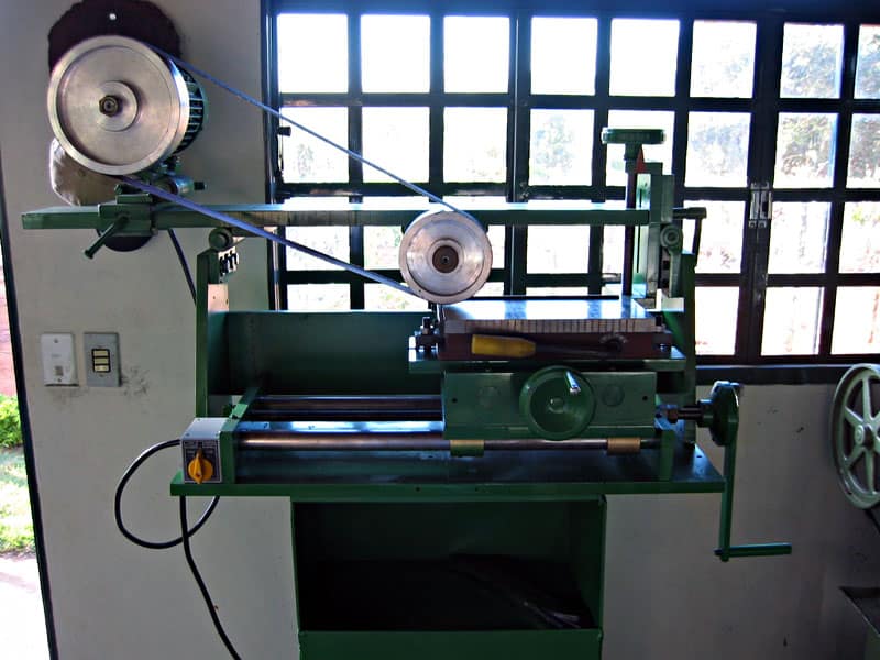 A metal lathe machine in a home machine shop with a large window in the background, showcasing its various components like the chuck, tool post, and tailstock.