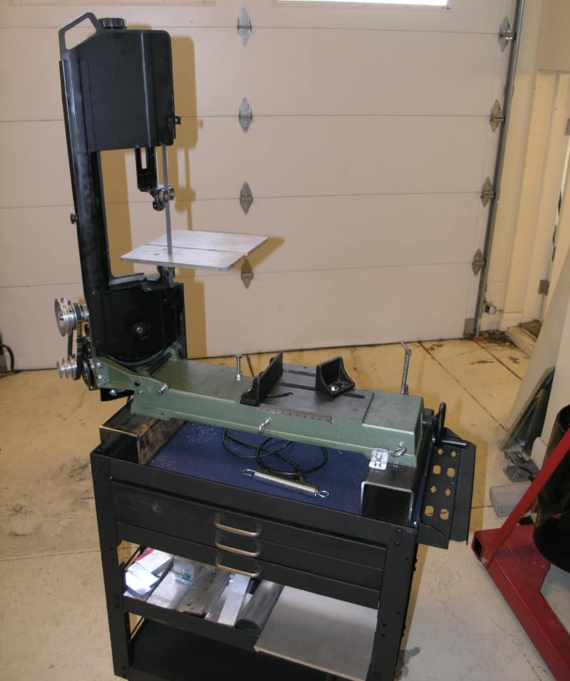 Black and green bandsaw on black cart in front of garage door.