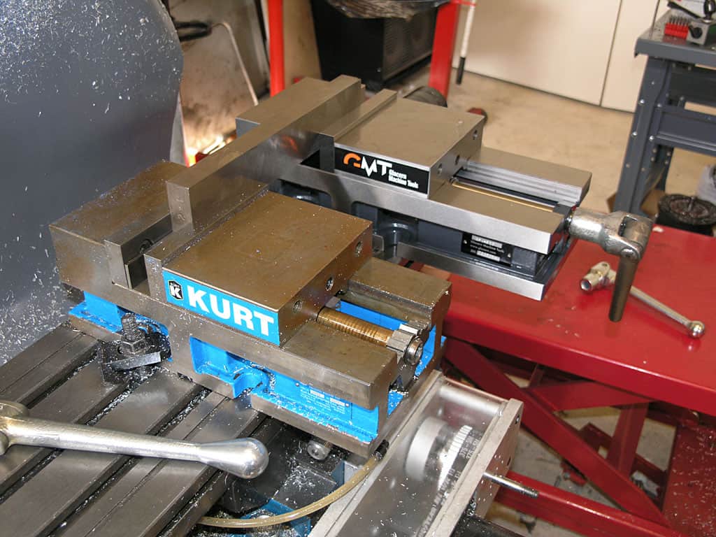 Two heavy-duty vices on a workbench by Kurt Manufacturing and CMT.