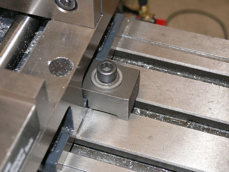 Metal machine component with silver metal piece and screw/bolt centered among surrounding metal parts.
