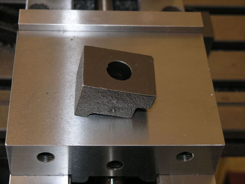 Square metal object with a central hole on top of a metal surface.