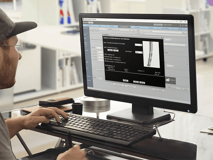 Man sitting at desk in front of two computer monitors displaying CAD modeling program.