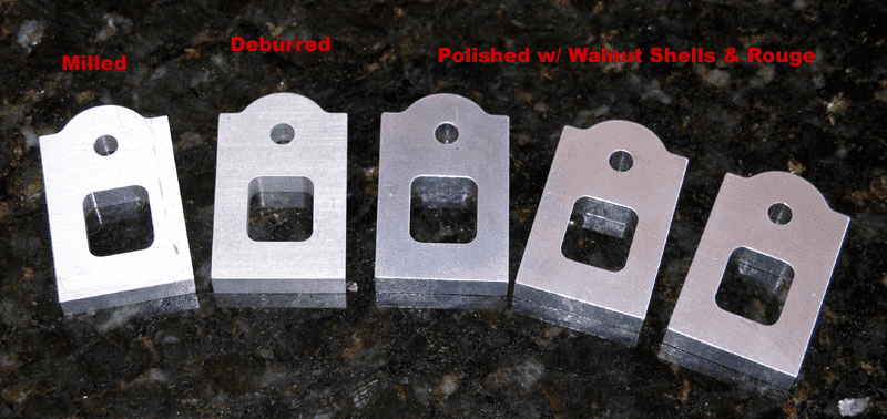 Metal parts with varying surface finishes on a black granite countertop, labeled Milled, Deburred, Polished w/Walnut Shells & Rouge.