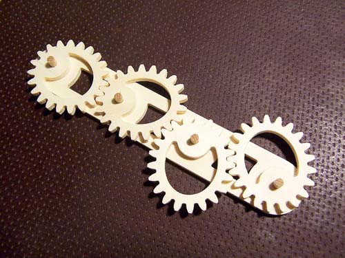 Four interlocking white plastic gears designed using gear design software on a dark brown textured surface.