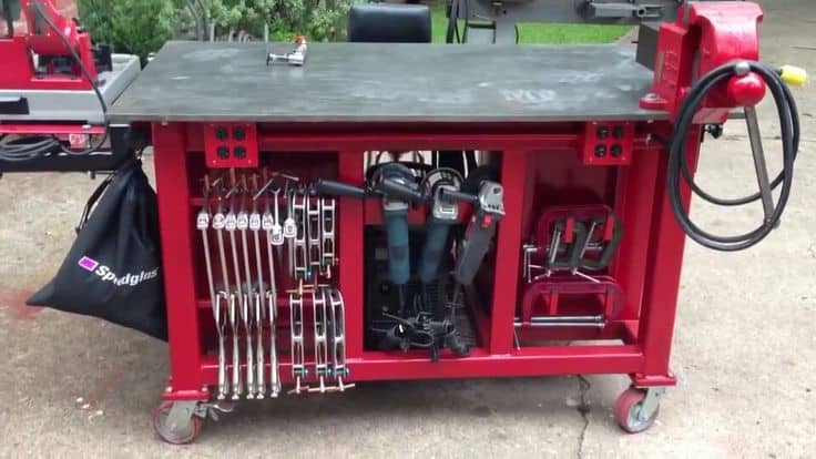 A red mobile tool cart equipped with various tools, including wrenches and power tools, parked on a concrete surface and ideal for DIY welding projects.