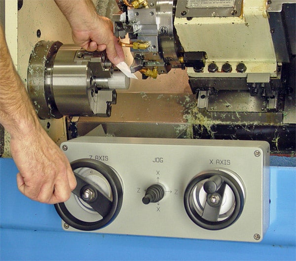 A person operating a CNC conversion lathe machine, adjusting the control panel with labeled knobs for precision in a workshop setting.