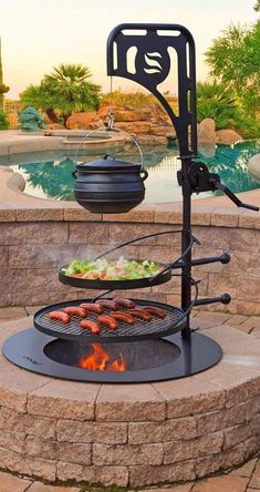 Black cast iron grill with hanging pot over an open flame on a circular stone base.