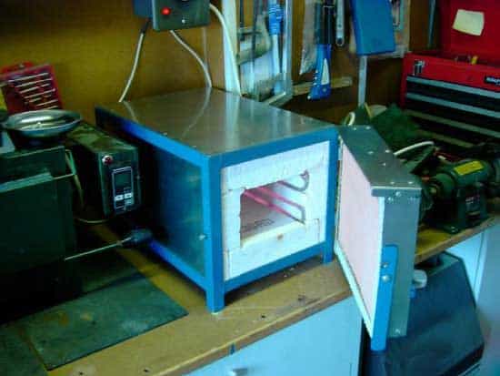 Blue furnace on wooden workbench in machine shop or metal fabrication facility.