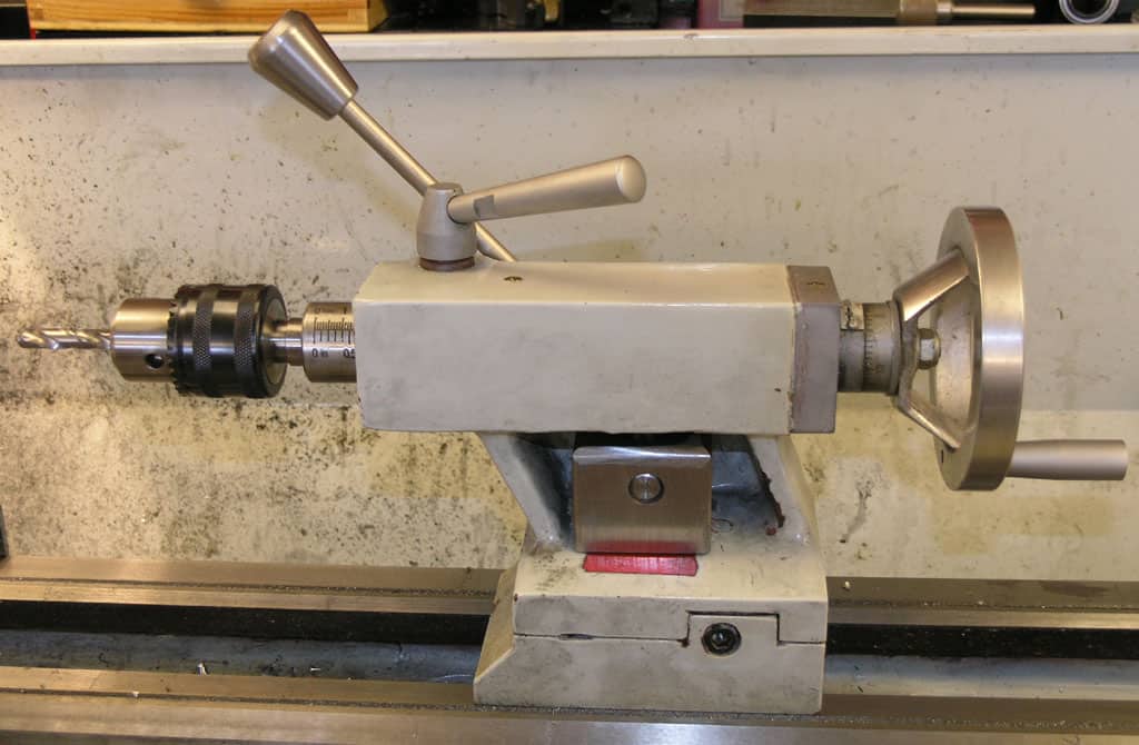 An industrial mini-lathe on a workshop counter, featuring a chuck, levers, and a tailstock, with visible metal shavings.