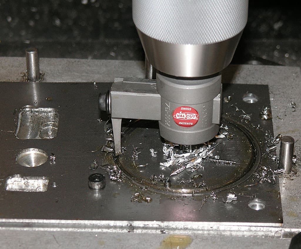 Swiss-made Valcut drill bit on a metalworking machine amidst scattered metal shavings.