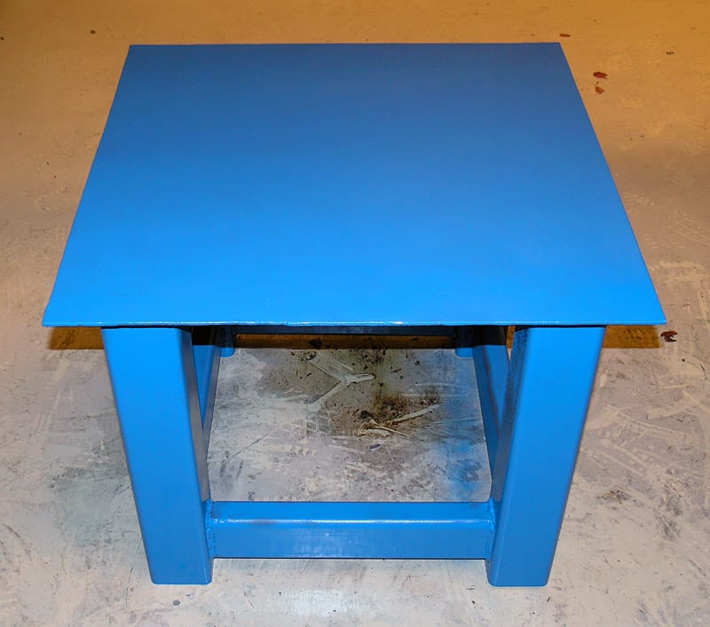 Small blue wooden/plastic table on concrete floor with bright blue coat.