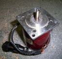 Red electrical component with silver top and cylindrical protrusion on black cord.