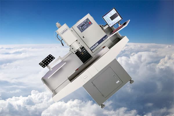 A computer-aided manufacturing workstation with control panel and gray cabinet, set against a cloudy sky background.