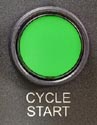 Green "cycle start" button on a dark background, used in CNC machining.