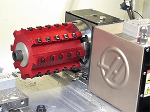 A red cylinder on a flat surface next to a silver machine with a circular indentation on a white wall.