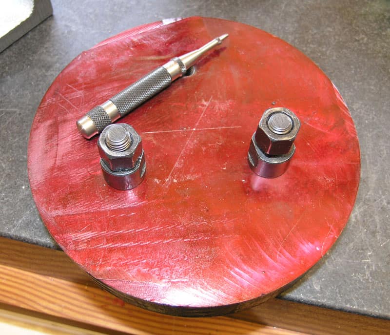 Red circular tool with three metal studs and small silver handheld device on top.