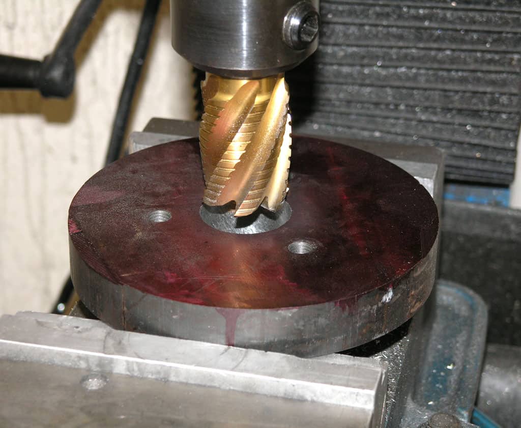 Metalworking tool with gold spiral cutting edge and dark red base on a factory workshop floor.