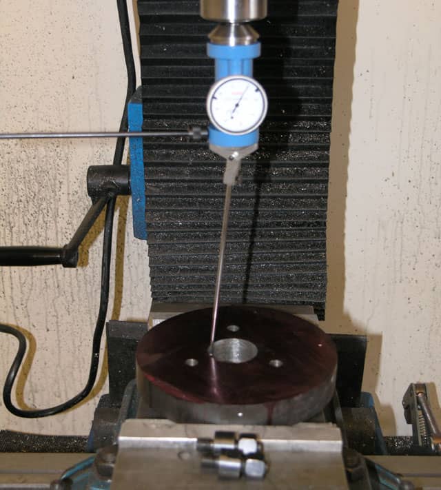 Precision instrument with a dial gauge on a stand, on a metal surface with surrounding components.