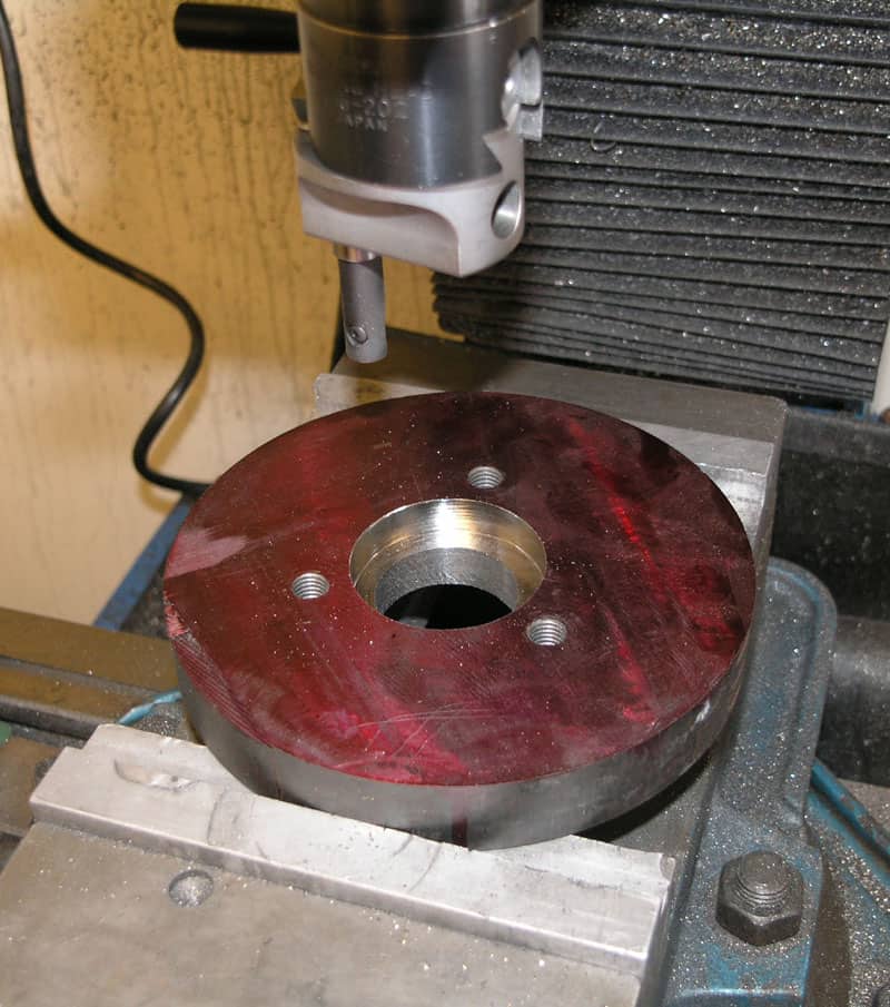 Metal part with red finish being machined on drill press or milling machine.