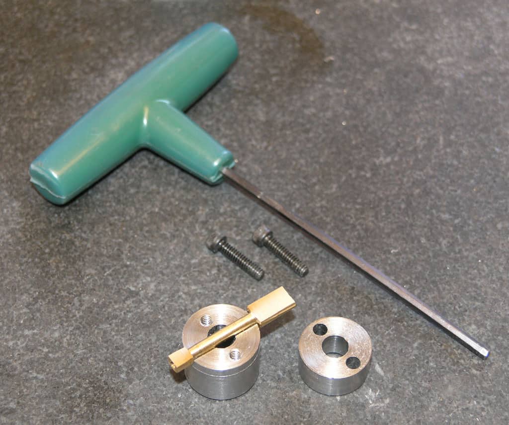 A green-handled screwdriver with a disassembled metal chuck and two connecting rods arranged on a gray surface.