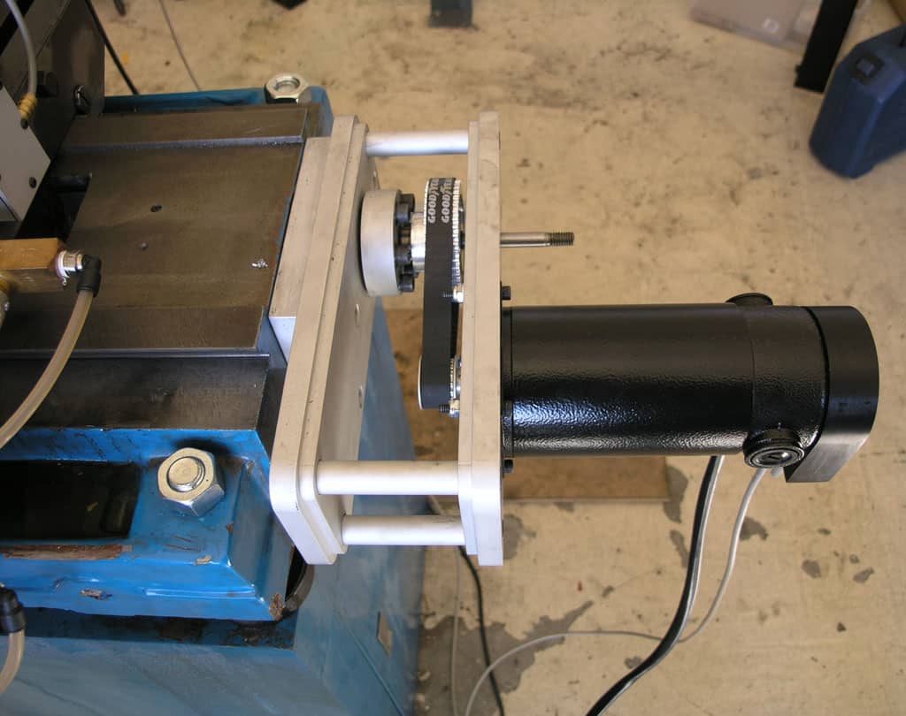 Machine with black cylindrical component on blue metal base and screws on concrete floor.