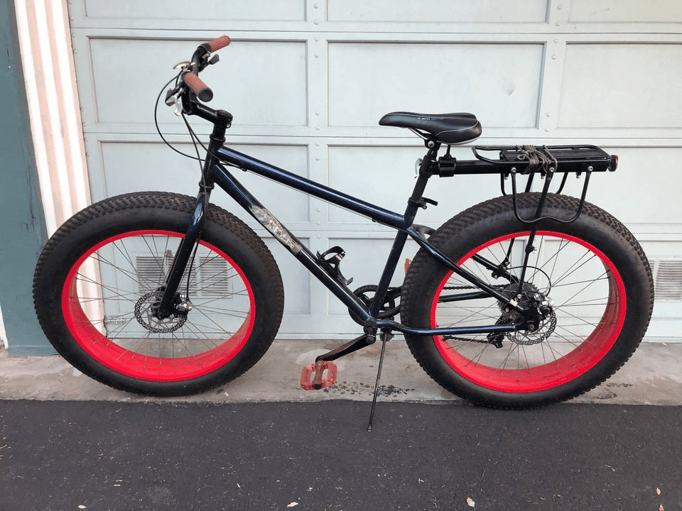 A black fat tire e-bike with red rims parked in front of a garage door.