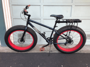 Black bicycle with red rims in front of a white garage door.