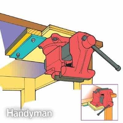 Red bench vise on wooden workbench with adjustable jaws and metal bar.