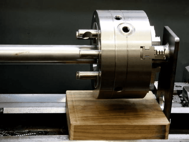 A stainless steel shaft with two small protrusions attached to a lathe, made of high-quality material.