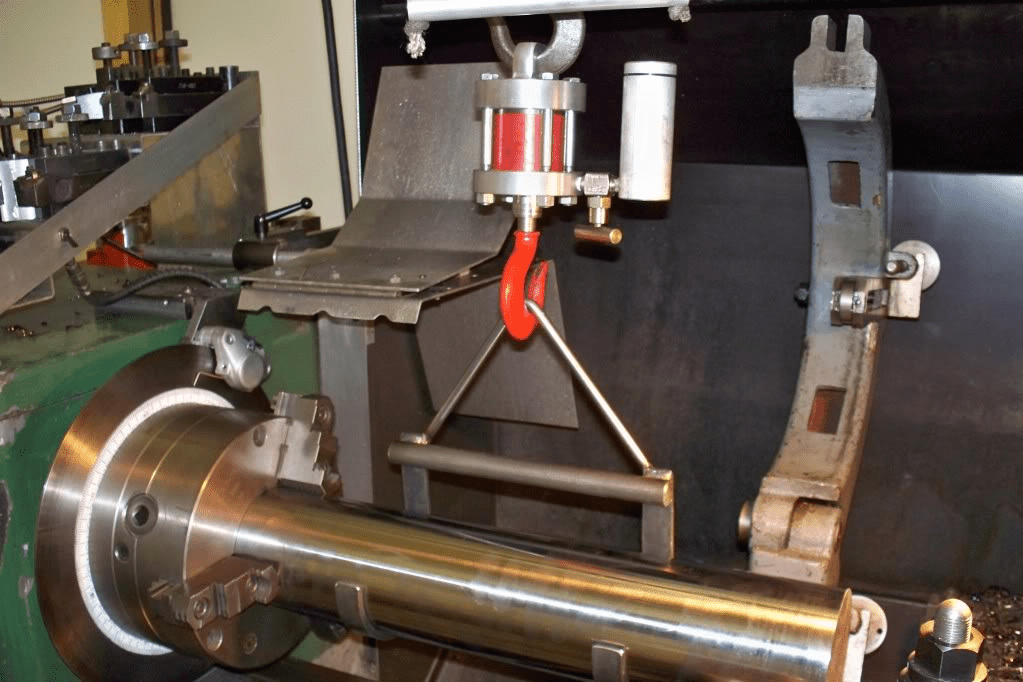 Metalworking lathe with tools and parts attached on a green machine in a workshop.