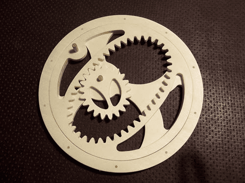 A close-up of a white gear with internal teeth and central hole set against a dark background.